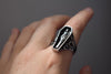 Silver ring with a coffin and figure design on a hand against a gray background